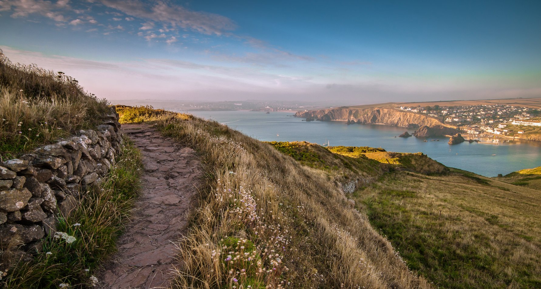 Landscape photo from the south west coast path at Bolt Tail across fields and the sea to coastal cliffs and Hope Cove