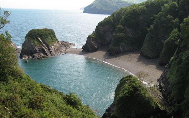 Photo looking down on sea and beach with rocky cliffs behind