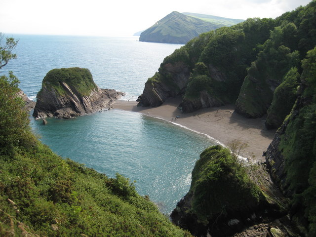 Photo looking down on sea and beach with rocky cliffs behind