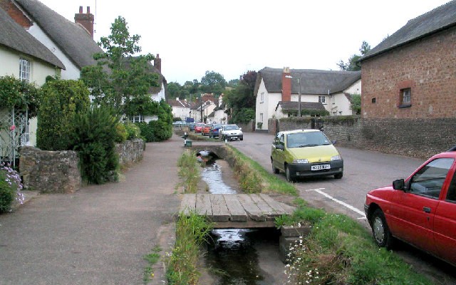 Photo of a street through Otterton lined with thatched cottages and a small stream