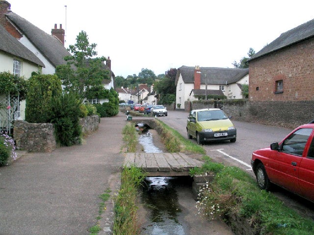 Photo of a street through Otterton lined with thatched cottages and a small stream