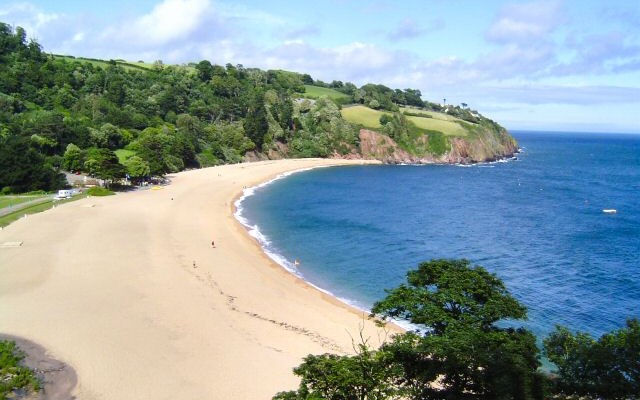 Photo across a long beach towards wooded coastal hillside at Blackpool Sands