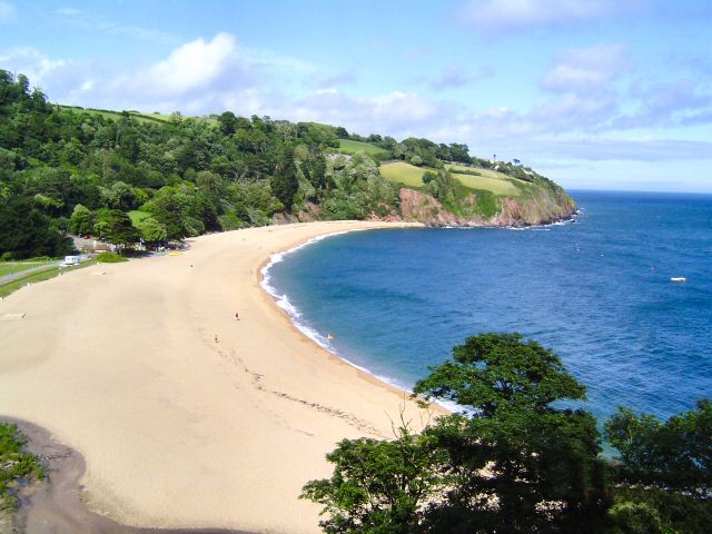 Photo across a long beach towards wooded coastal hillside at Blackpool Sands