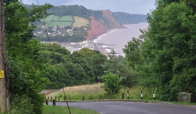 Photo looking down into Sidmouth from Peak Hill with the town in the bottom of the valley and the sea and red cliffs in the background