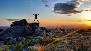 Person jumping off rocks with sunset in background