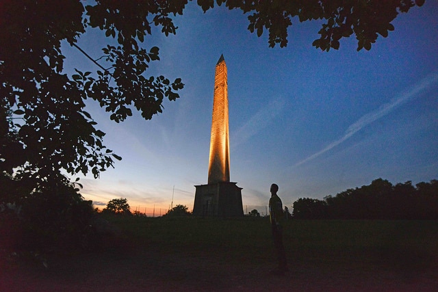 Photo of a man standing in front of the Wellington Monument at night