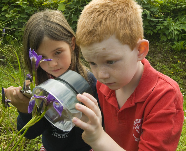 Photo of two children looking at a flower through a magnifying lens